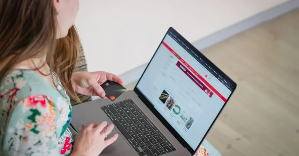 Woman in floral dress shopping online with a laptop and credit card indoors.