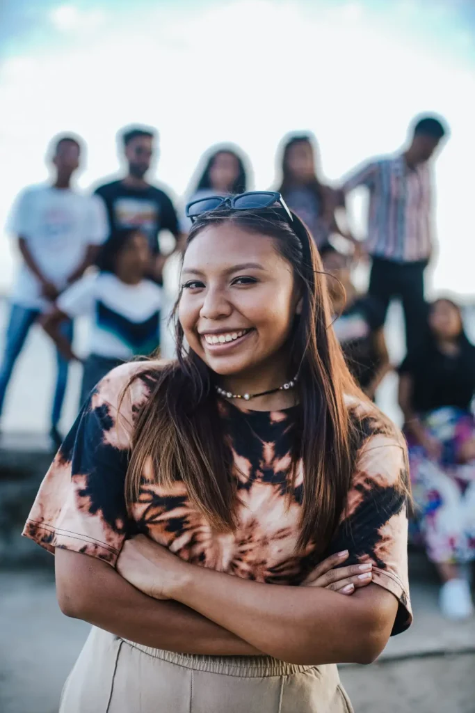 A cheerful woman stands with her arms crossed, surrounded by friends, showcasing happiness and camaraderie.